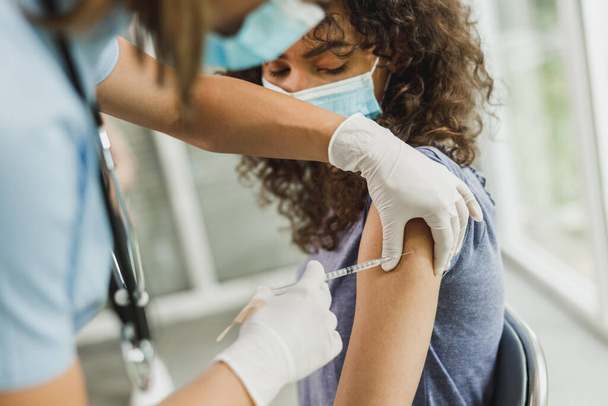 Zbliżenie Afroamerykańskiej nastolatki otrzymującej szczepionkę z powodu pandemii koronawirusowej. - Zdjęcie, obraz