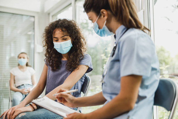 Nurse talking to African American female teenager and taking notes before vaccination against coronavirus. - Photo, Image