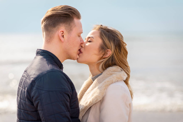 Young couple kissing in love outdoor.Stunning sensual outdoor portrait of young stylish fashion couple posing in spring,autumn sea background. - Photo, Image