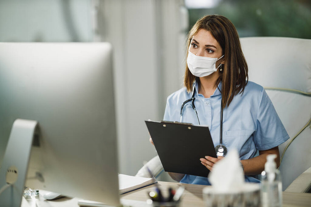 Eine Krankenschwester mit schützender Gesichtsmaske telefoniert während der Coronavirus-Pandemie mit einer Patientin am Computer. - Foto, Bild