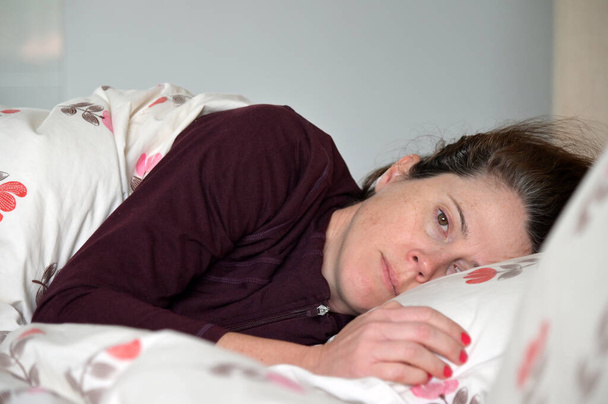 Donna adulta (età femminile 30-40 anni) sdraiata a letto con depressione guardando la macchina fotografica. - Foto, immagini