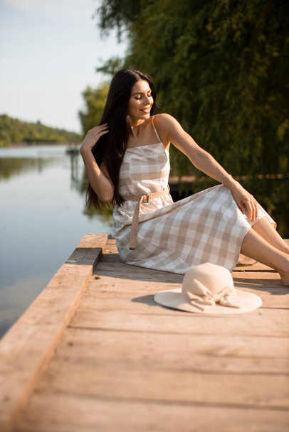Sakin gölün kıyısındaki tahta iskelede rahatlatıcı genç bir kadın. - Fotoğraf, Görsel