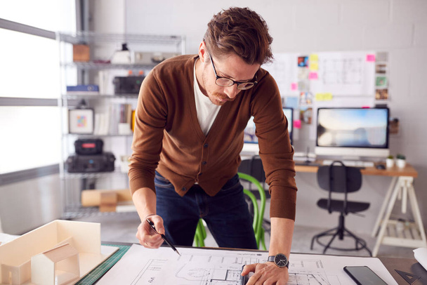 Male Architect Standing At Desk In Office Amending Building Plans - Fotó, kép