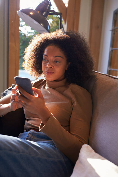 Woman Relaxing In Chair At Home Checking Social Media On Mobile Phone - Photo, image