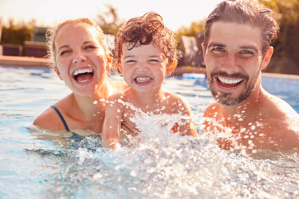 Portrait Of Family With Young Son Having Fun On Summer Vacation Splashing In Outdoor Swimming Pool - Fotografie, Obrázek