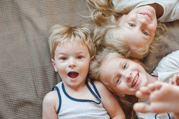 Portret trojga dzieci leżących na łóżku. Siostry i brat uśmiechający się patrząc w kamerę - Zdjęcie, obraz