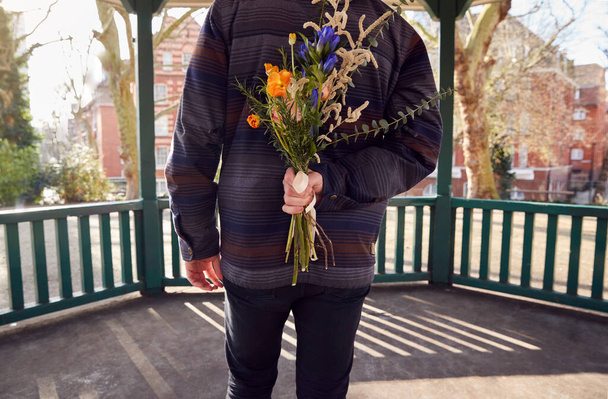 Romantic Man With Bouquet Of Flowers Behind Back Surprising Young Woman As They Meet In City Park - Foto, Imagen