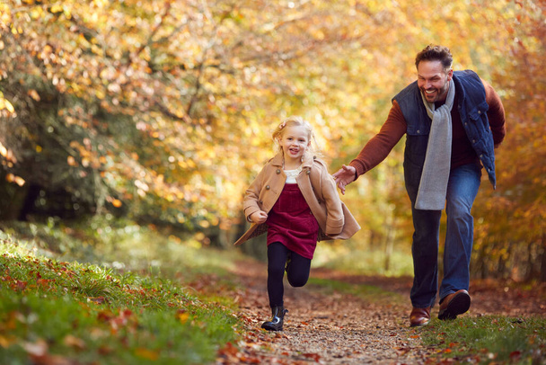 Father And Daughter On Family Walk Along Track In Autumn Countryside With Girl Running Ahead - Photo, Image