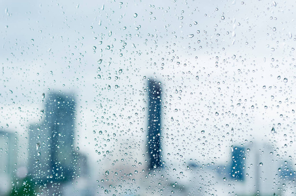Regentropfen auf Glasfenster zur Tageszeit in der Monsunzeit mit verschwommenem Hintergrund städtischer Gebäude. - Foto, Bild