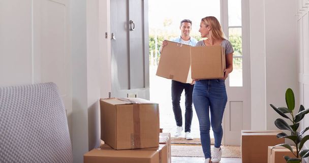 Excited Couple Carrying Boxes Through Front Door Of New Home On Moving Day - Photo, image