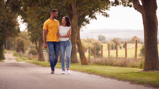Front View Of Loving Couple Hugging As They Walk Along Track Through Countryside - Photo, image