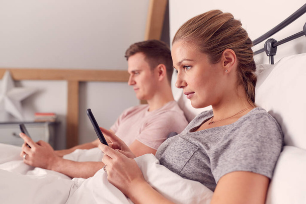 Pizsamát viselő pár mobiltelefon-függőség az ágyban fekve, és nem kommunikálnak. - Fotó, kép