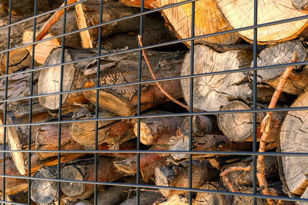 Brennholz hinter einem schwarzen Gitter aus Eisen. Ort der Lagerung von Brennholz - Foto, Bild