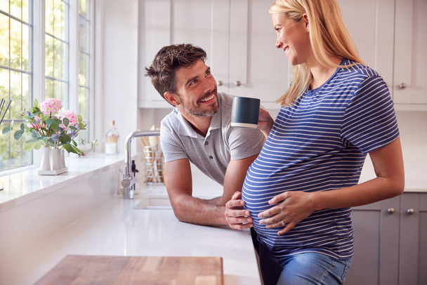 Couple In Kitchen With Man Chatting To Pregnant Woman As She Drinks Cup Of Coffee - Foto, Imagem