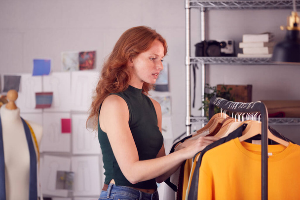 Female Owner Of Fashion Business Checking Clothing Samples On Rail In Studio - Foto, Imagem