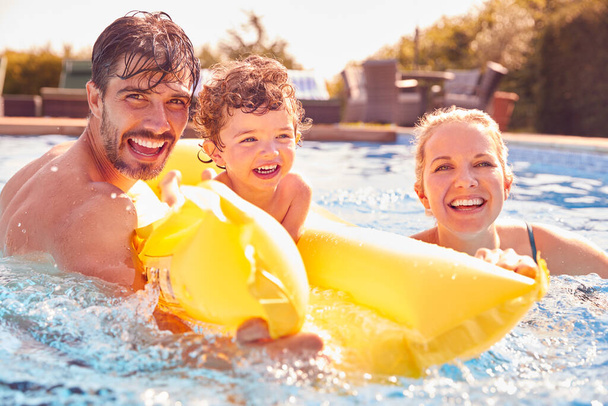 Family With Young Son Having Fun With Inflatable On Summer Vacation In Outdoor Swimming Pool - Foto, Imagem