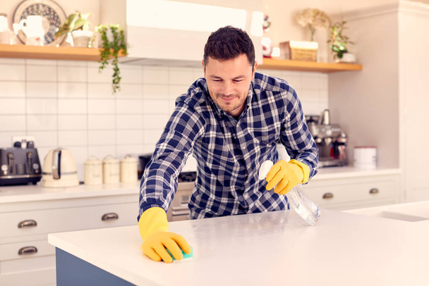 Man At Home In Kitchen Doing Housework And Cleaning Counter Surface With Spray - Fotoğraf, Görsel