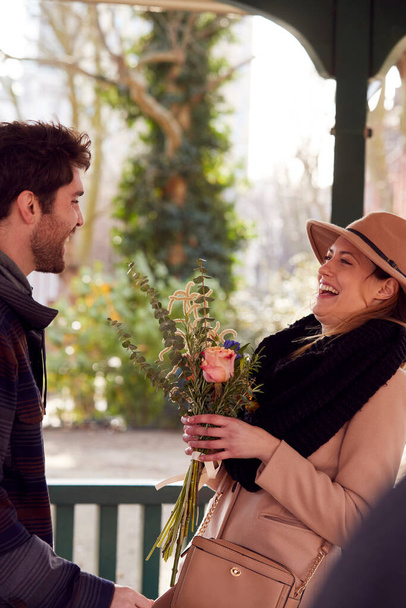 Romantic Man Surprising Young Woman With Bouquet Of Flowers As They Meet In City Park - 写真・画像
