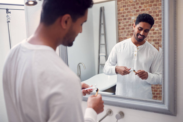 Man Wearing Pyjamas At Home In Modern Bathroom Brushing Teeth In Mirror - Foto, immagini