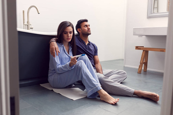 Disappointed Couple Sitting On Floor In Bathroom At Home With Negative Home Pregnancy Test - Foto, immagini