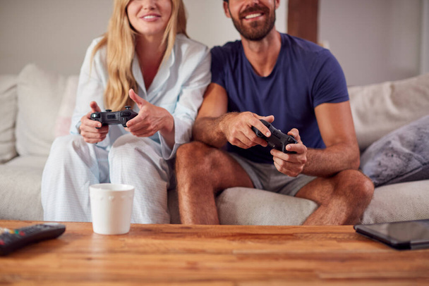 Couple Wearing Pyjamas Sitting On Sofa Playing Computer Game Together - Foto, immagini