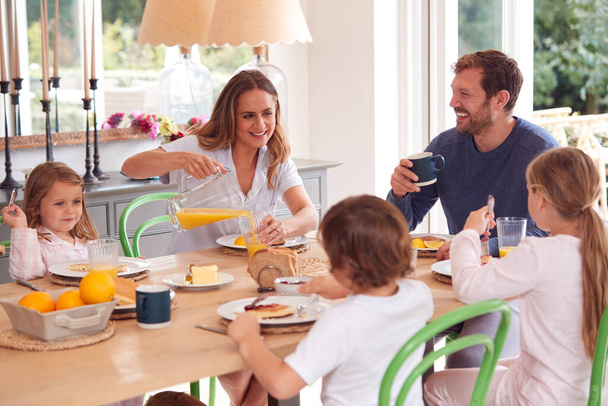 Family Wearing Pyjamas Sitting Around Table Enjoying Pancake Breakfast Together - Fotoğraf, Görsel