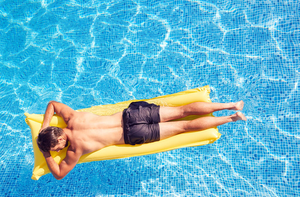 Overhead Shot Of Man In Swim Shorts Floating On Air Bed On Summer Vacation In Outdoor Swimming Pool - 写真・画像