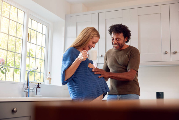 Couple With Pregnant Wife In Kitchen With Husband Touching His Wife's Bump - Photo, image