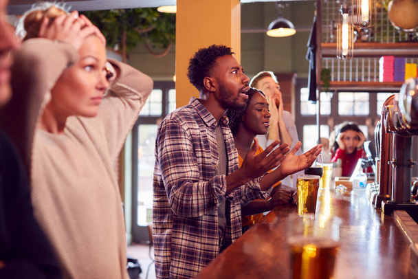 Group Of Disappointed Customers In Sports Bar Watching Sporting Event On Television - Foto, Imagen
