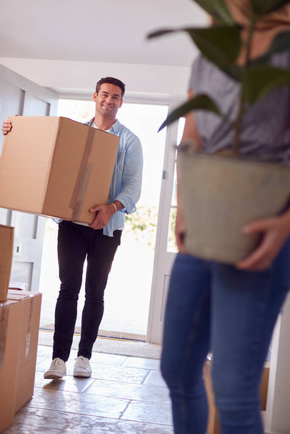 Excited Couple Carrying Boxes And Plant Through Front Door Of New Home On Moving Day - Foto, Imagem