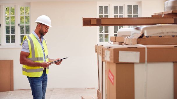 Builder Wearing Hard Hat With Clipboard Checking Delivery Of New Kitchen Units Inside Property - 写真・画像