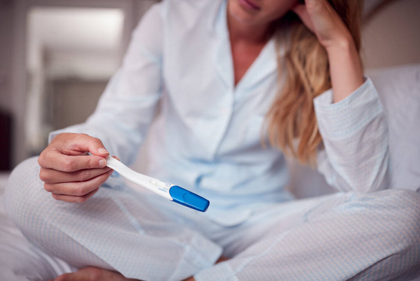 Close Up Of Nešťastná žena na sobě pyžama v ložnici držení těhotenský test - Fotografie, Obrázek
