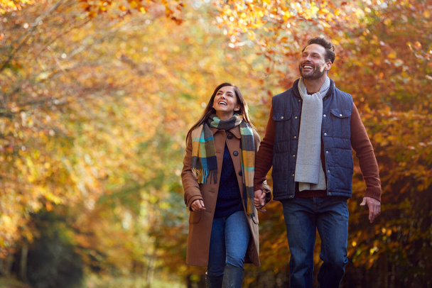 Loving Mature Couple Holding Hands Walking Along Track In Autumn Countryside - Foto, afbeelding