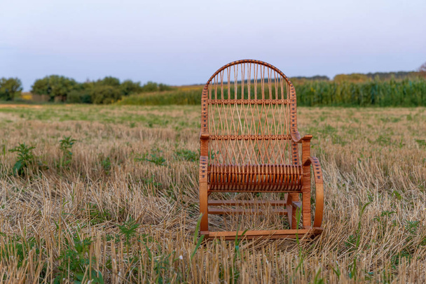 Пустое кресло-качалка на скошенном поле на закате. Плетёное кресло-качалка. Спокойный момент. Отдых вечером в сельской местности - Фото, изображение
