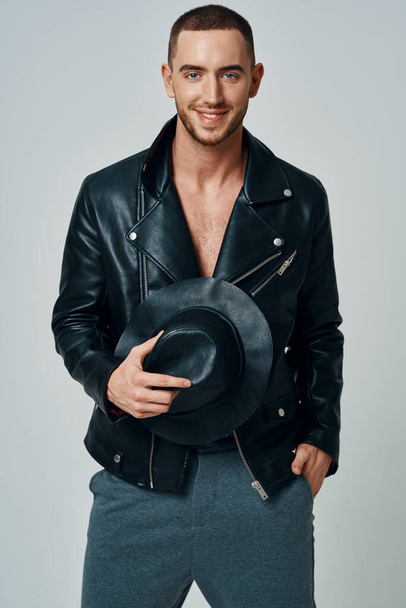 man in black leather jacket hat posing fashion confident light background - Foto, afbeelding