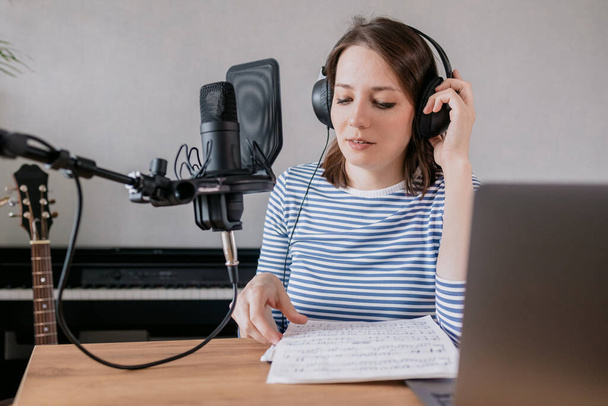 the stylish and educated caucasian woman records podcasts in a recording studio or in her home. the European millennial woman creates audio content or records text, records an audio book or radio show - Foto, Bild