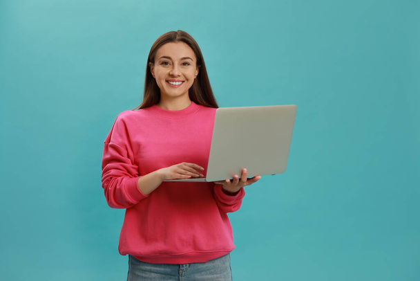 Young woman with modern laptop on light blue background - Foto, afbeelding