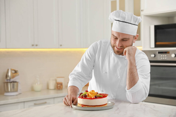 Happy professional confectioner with delicious cake at table in kitchen - Фото, зображення