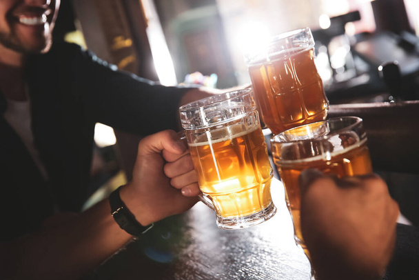 Friends clinking glasses with beer in pub, closeup - Fotó, kép