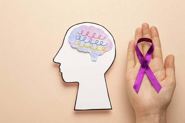 Woman holding purple ribbon near paper human head cutout over beige background, top view. Epilepsy awareness - Foto, imagen