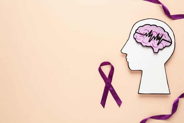 Human head cutout with brain near purple ribbons on beige background, flat lay. Epilepsy awareness - Фото, изображение