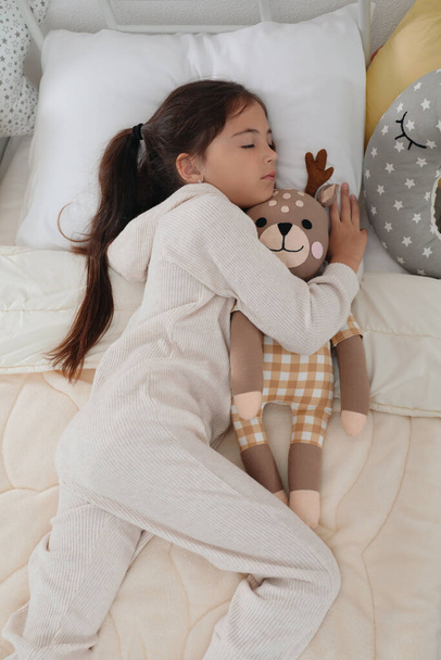 Cute girl in pajamas sleeping with toy deer at home - Фото, изображение