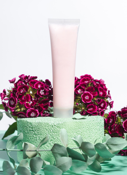 Bílé generické krém trubice na zeleném pódiu s růžovými květy - Fotografie, Obrázek