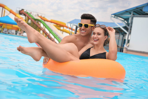 Pareja feliz con anillo inflable en piscina en parque acuático - Foto, Imagen