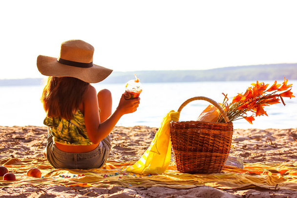 Kaunis teinityttö olkihattu päässä rannalla limonadi kädessä. Piknik joen rannikolla, ruudullinen, puinen paju kori oranssi lilja kukkia. Koulutyttö kesälomilla takaisin näkymä - Valokuva, kuva