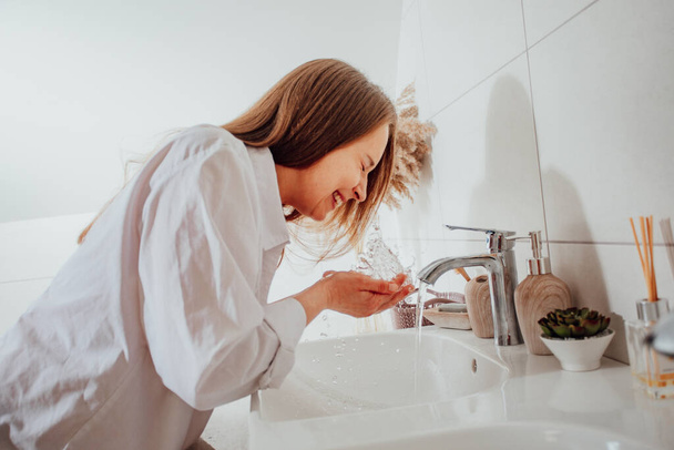 Femme éclaboussant visage avec de l'eau sur lavabo de salle de bains - Photo, image