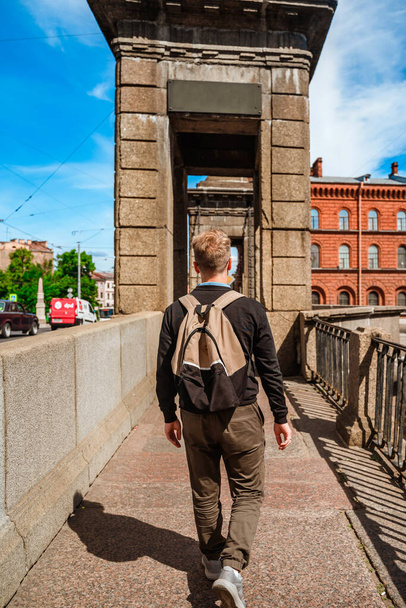  Egy fiatalember sétál Szentpéterváron a töltésen, gyönyörű kilátással a hidakra és csatornákra.. - Fotó, kép