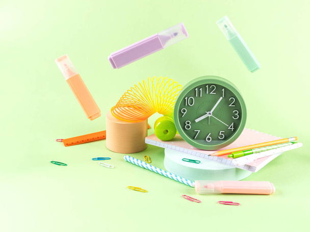 Back to school, office supply concept. Colorful stationery on green background with alarm clock - Photo, Image