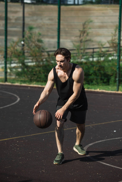 Muscular sportsman playing basketball on court outdoors  - Фото, изображение