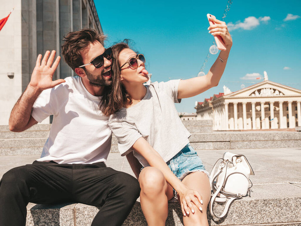 Portrait of smiling beautiful woman and her handsome boyfriend. Woman in casual summer clothes. Happy cheerful family. Female having fun. Couple posing in the street in sunglasses.Taking selfie - Zdjęcie, obraz